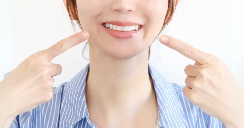 白い歯を見せて笑顔で口元を指さす女性