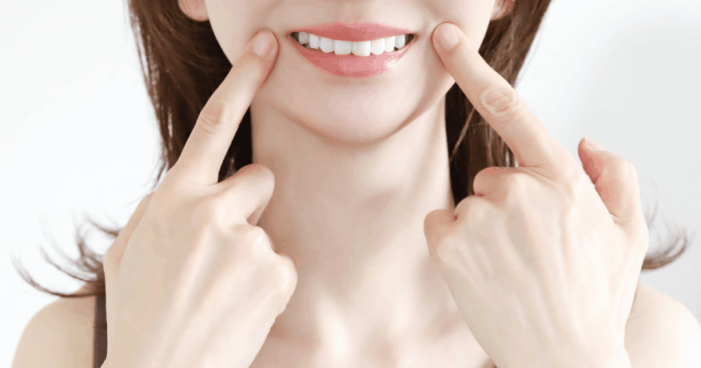 笑顔を指さして健康な歯を見せる女性